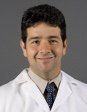 A man in a white coat and tie is smiling for the camera.