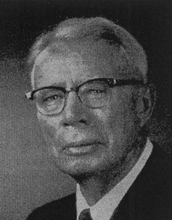 A black and white photo of a man wearing glasses and a suit and tie.