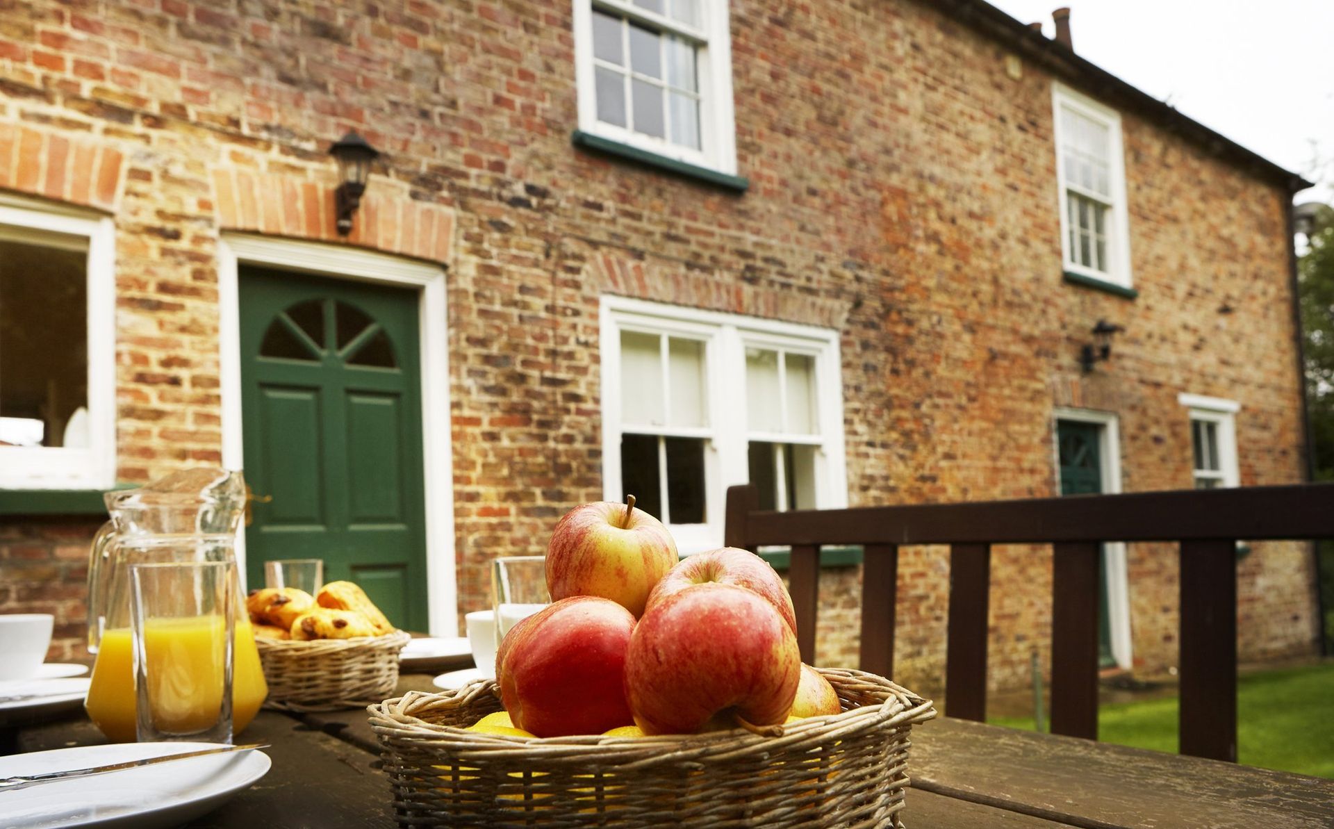 Brick cottage with a green door, a patio table with apples and orange juice.