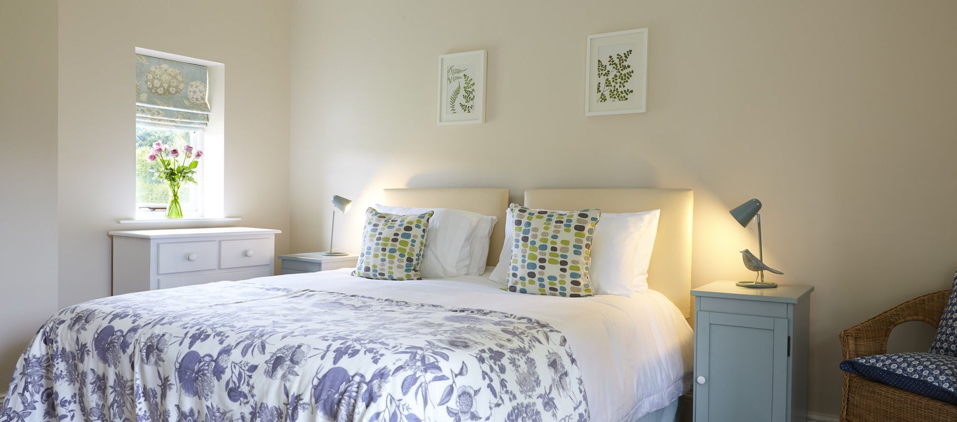 Cozy bedroom with a large bed, floral quilt, bedside tables, and artwork. Soft lighting.