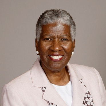 A woman with gray hair is smiling and wearing a pink jacket