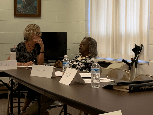Two women are sitting at a table with name cards and water bottles.