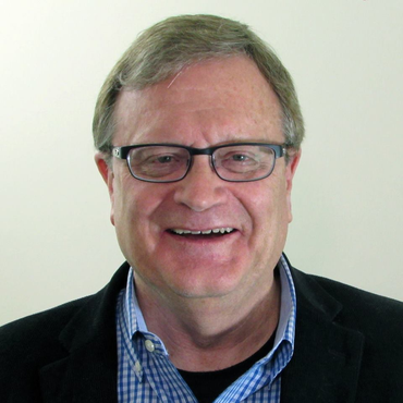 A man wearing glasses and a plaid shirt smiles for the camera