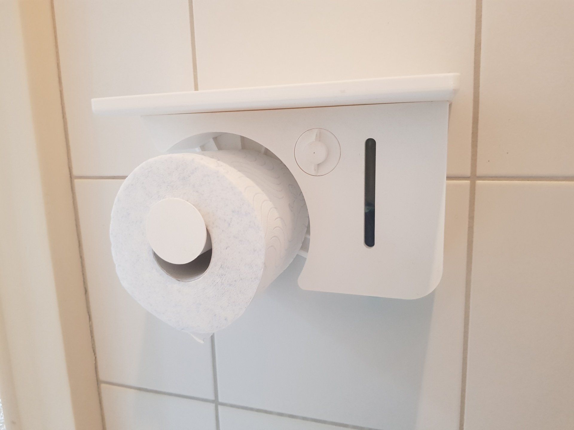 White toilet paper roll on a wall-mounted holder beside beige tiled wall.