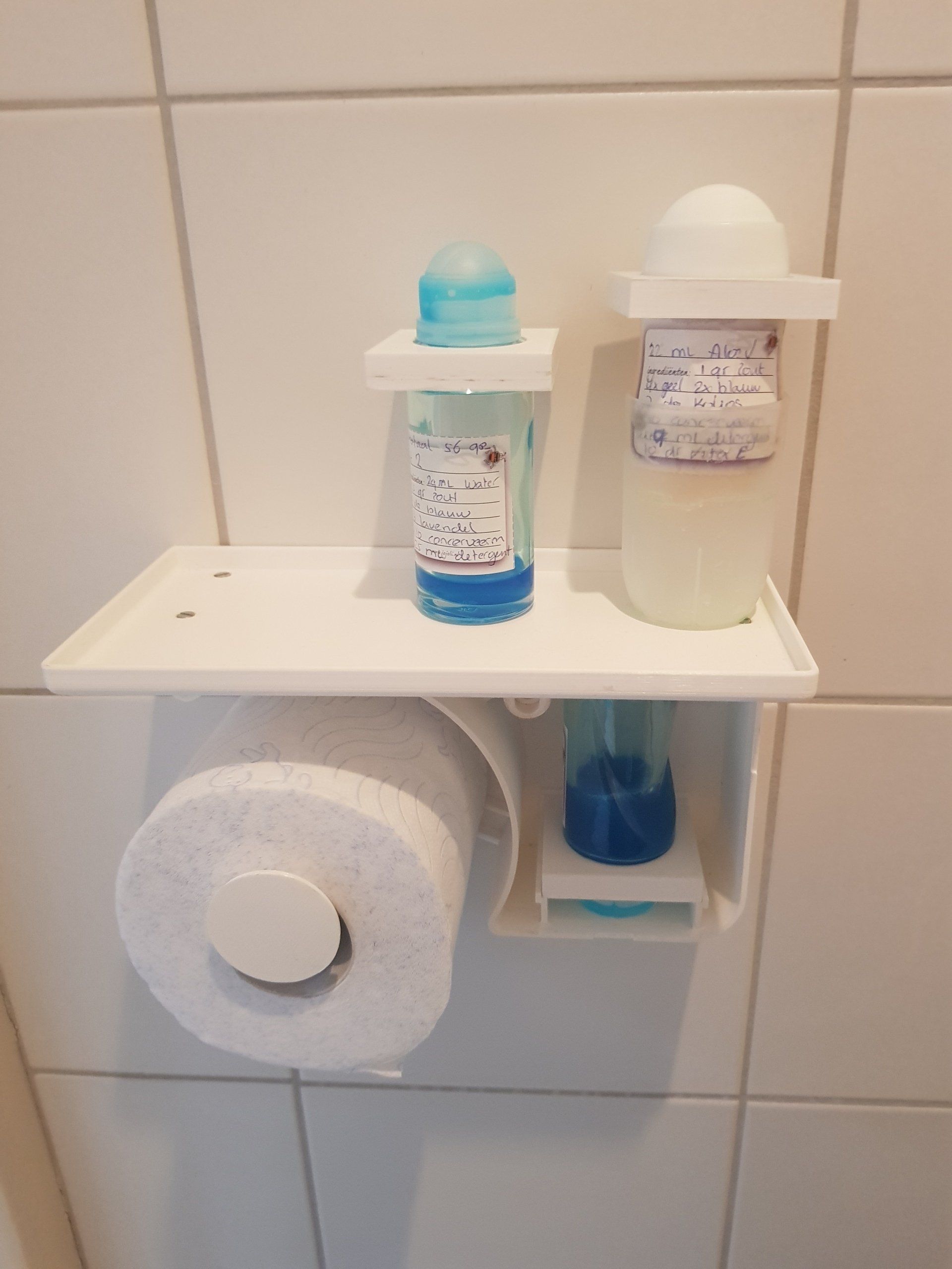 Bathroom shelf with two soap bottles and a toilet paper roll mounted on a tiled wall