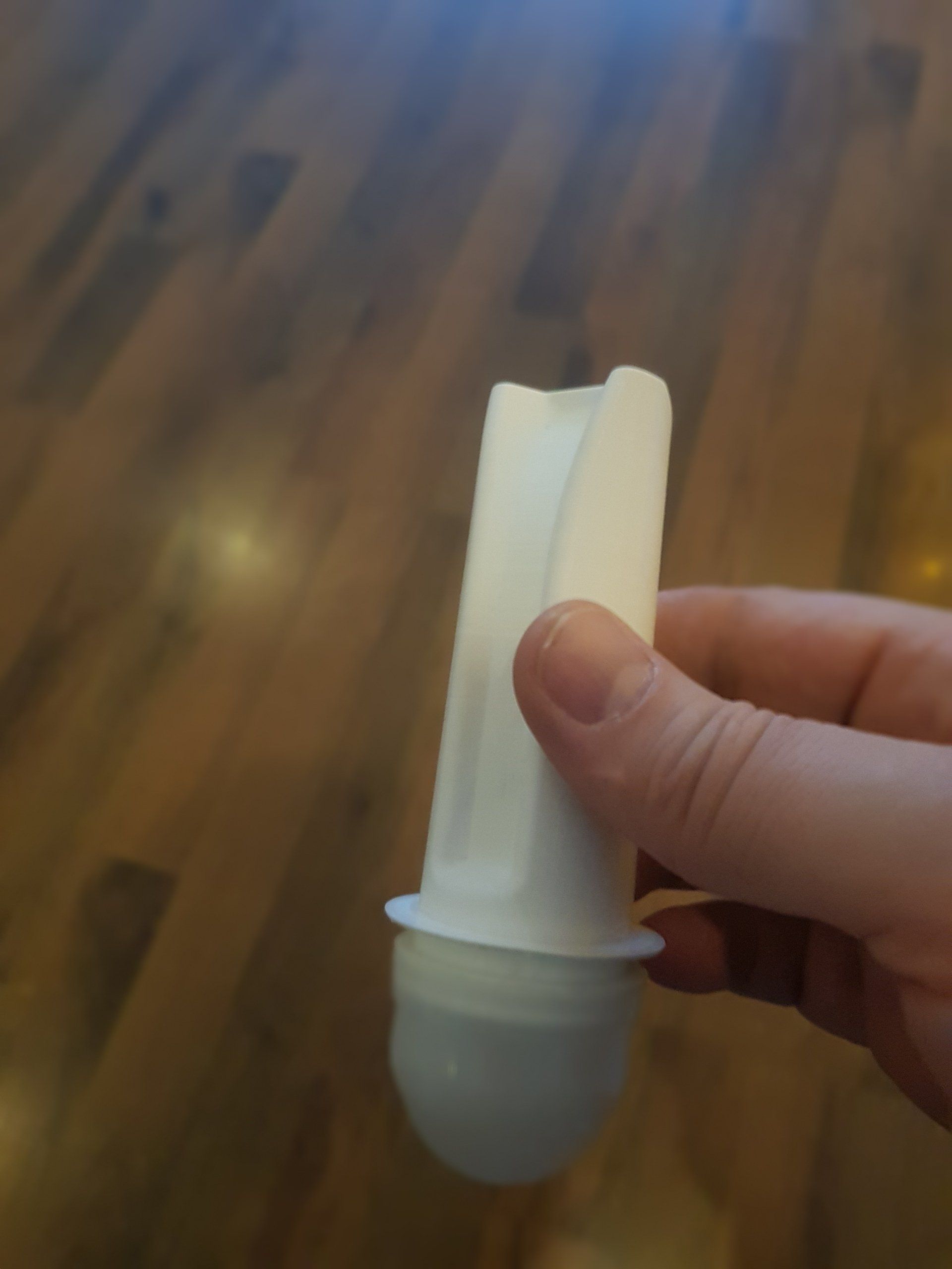 Hand holding a white plastic device with a rounded gray cap against a wooden floor.
