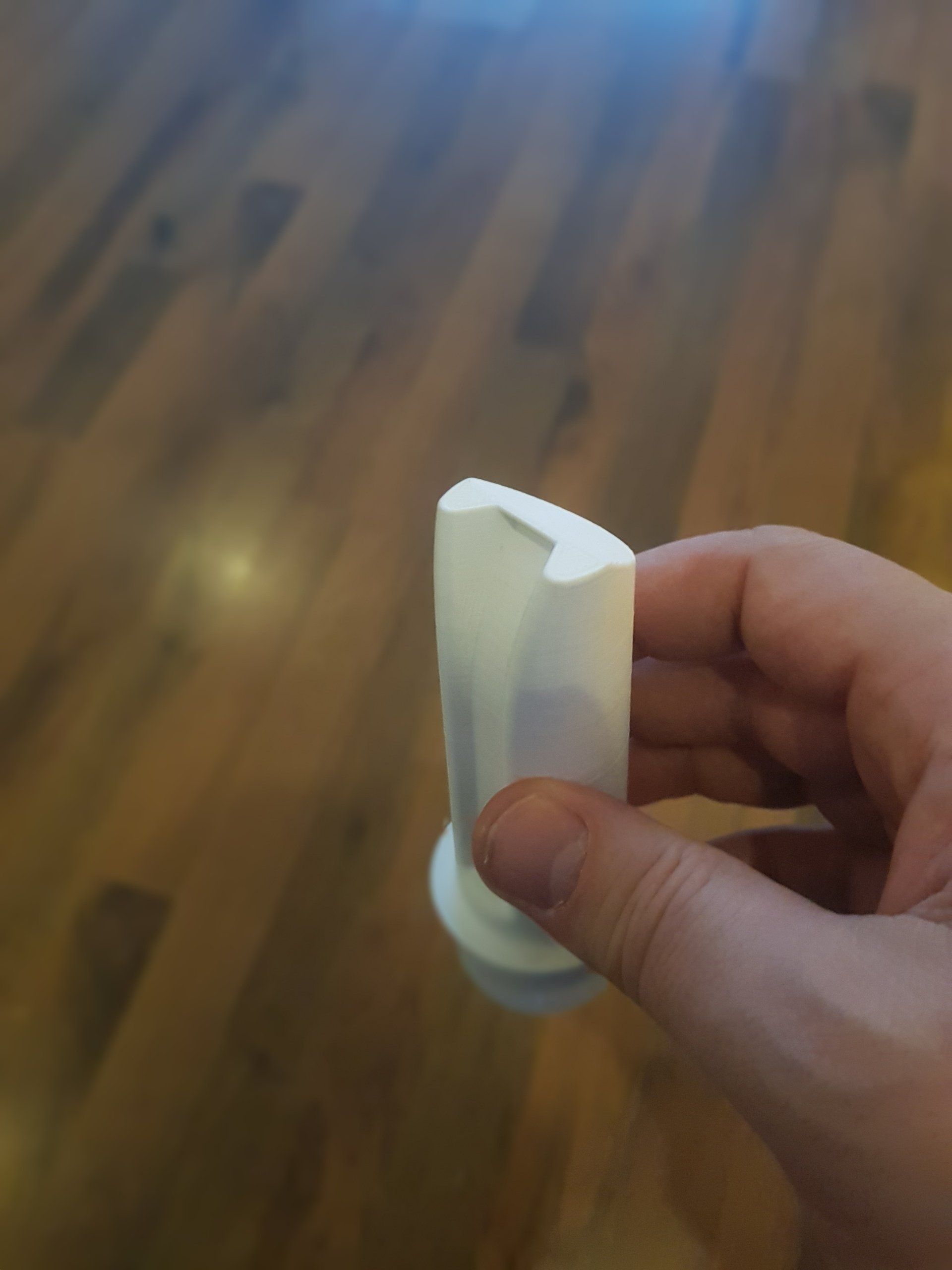 Hand holding a small white plastic object over a wooden floor