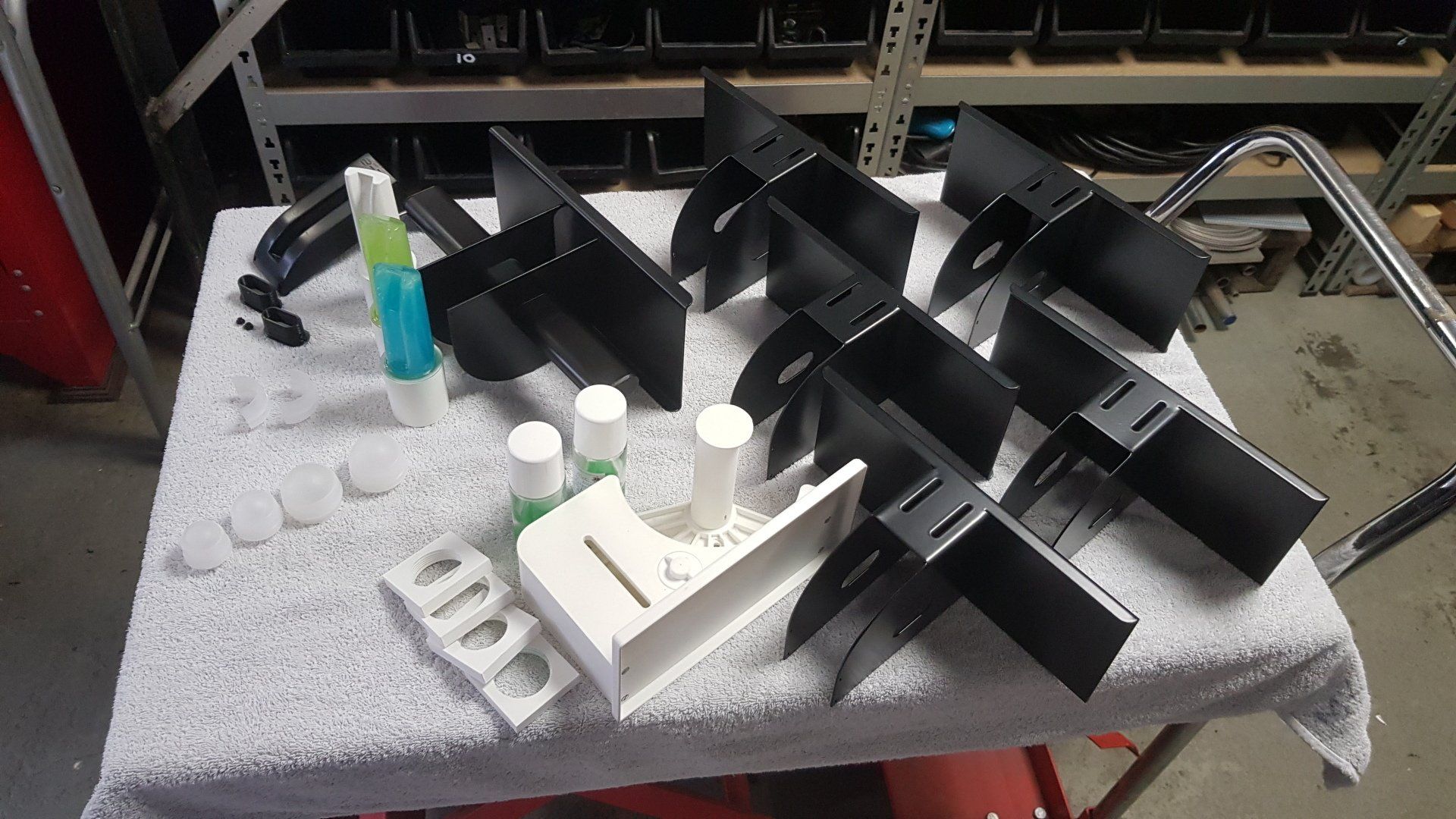 Assorted black and white tabletop objects and bottles arranged on a gray towel-covered workbench
