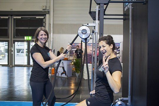 Two women exercising with a cable machine in a gym, smiling and making peace signs.
