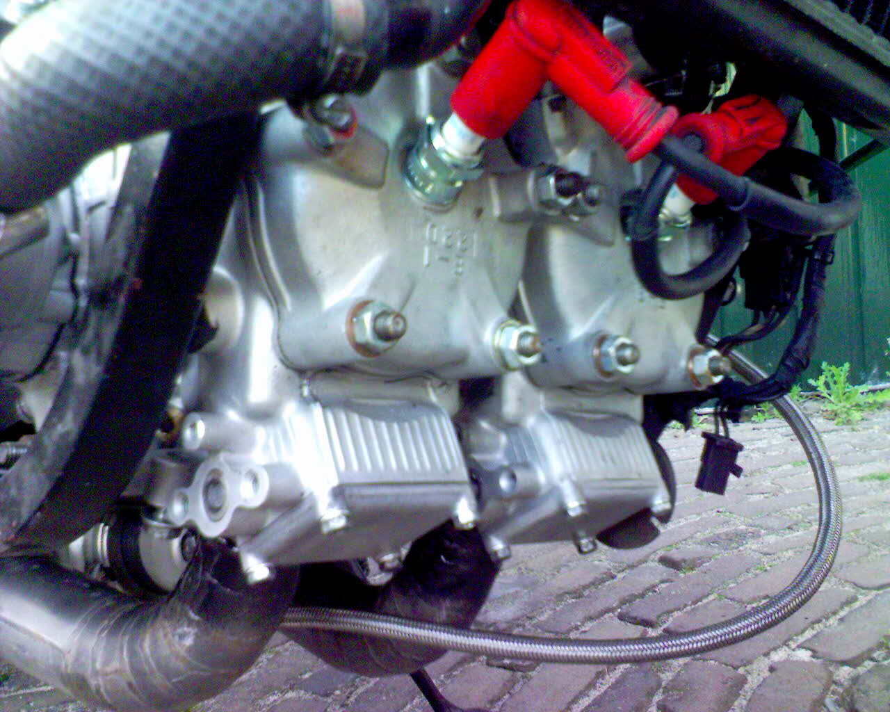 Close-up of a silver motorcycle engine with red hoses and black wiring.