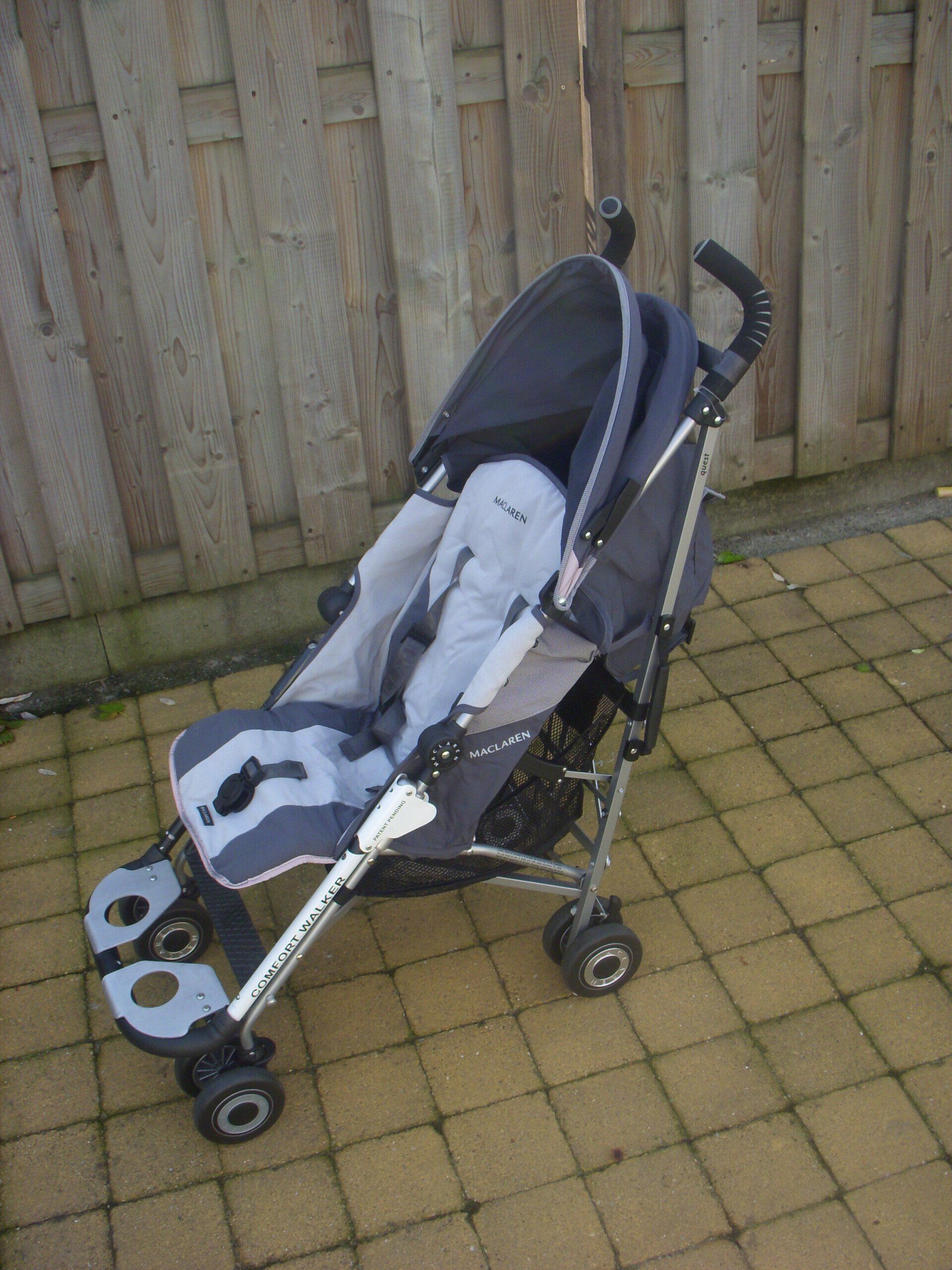 Empty black-and-gray baby stroller on a paved patio beside a wooden fence