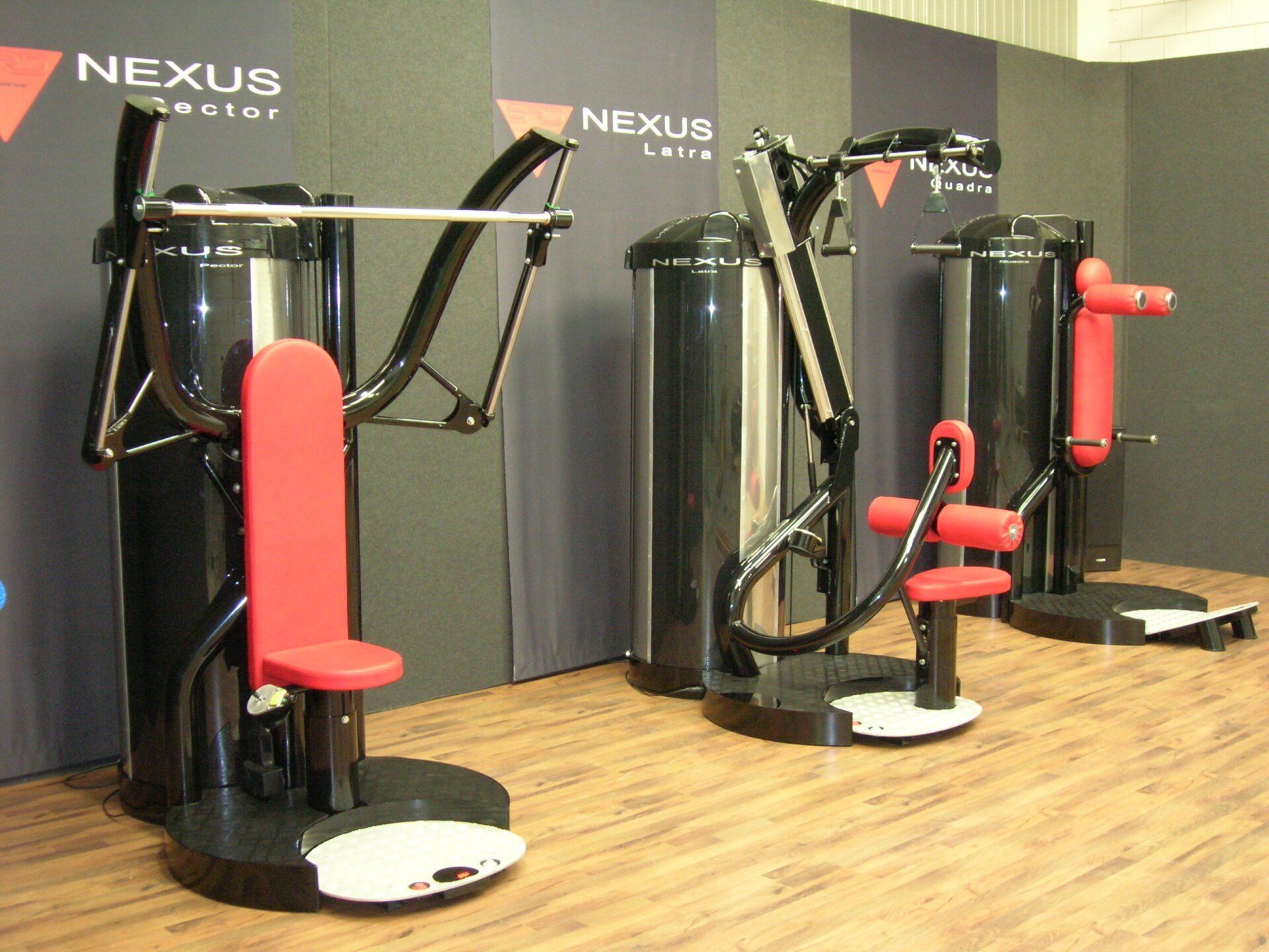 Gym machines with red seats in a fitness room with wood flooring and Nexus branding