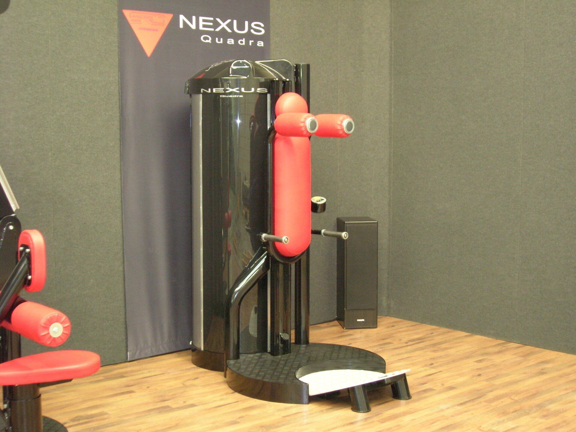 Nexus gym strength machine with red and black padding on a wood floor.