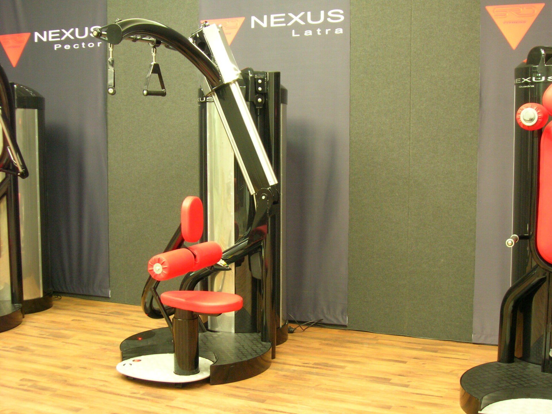 Red and black exercise machine displayed in a gym showroom with Nexus Fitness banners.