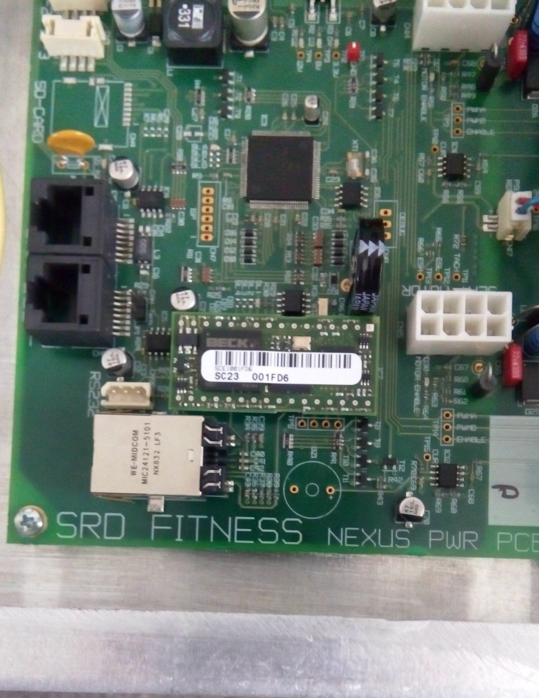 Close-up of a green circuit board with ports, chips, and connectors labeled “SRD Fitness Nexus”