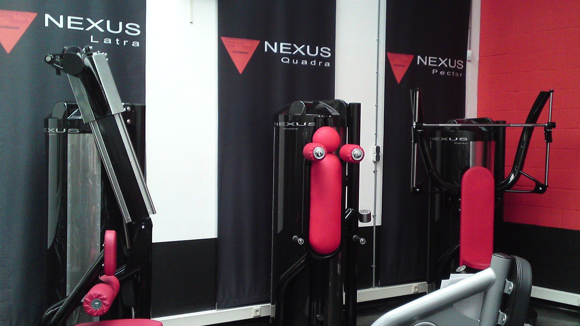 Nexus gym with three black-and-red exercise machines against a red wall
