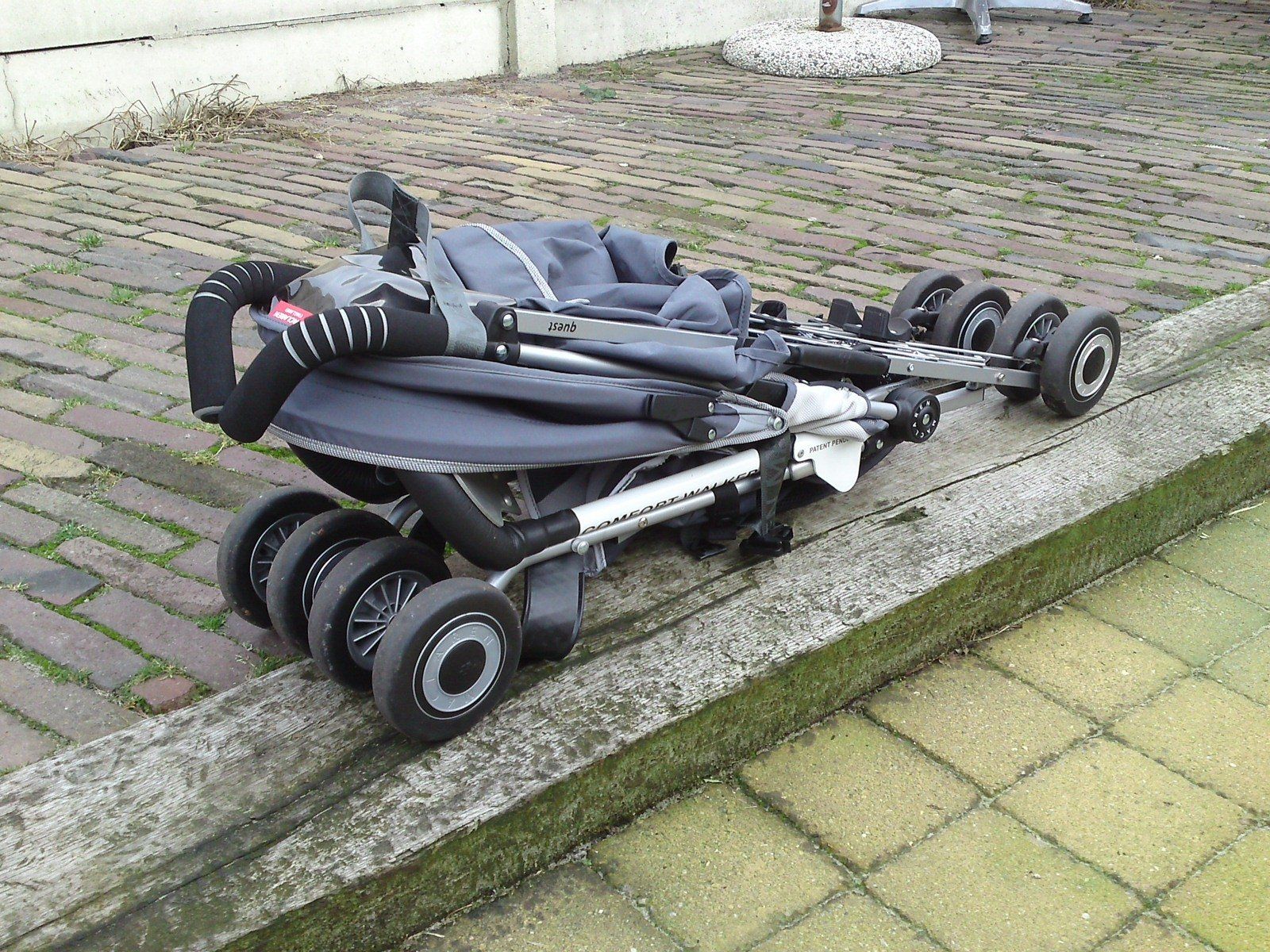 Folded black mobility scooter on a paved sidewalk beside a curb