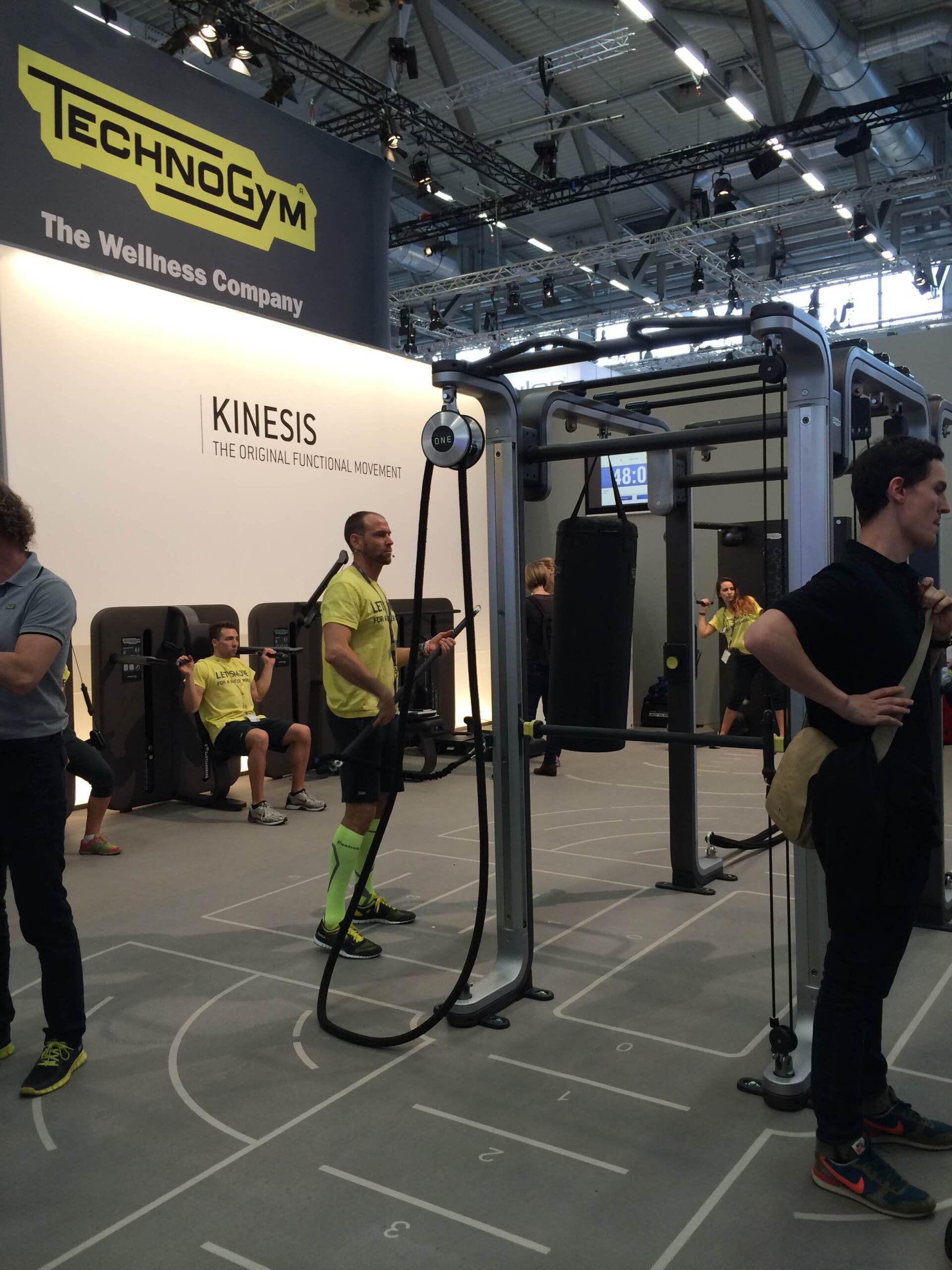 Indoor fitness expo booth with suspension training equipment and people demonstrating exercises