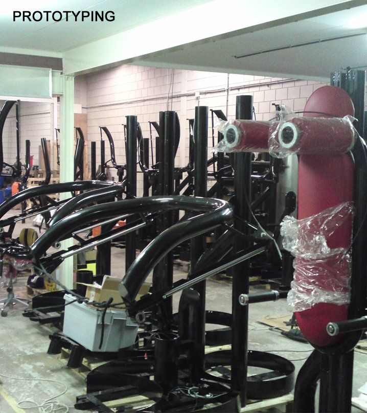 Factory prototype of a black metal robotic frame beside a red cylindrical machine in a workshop
