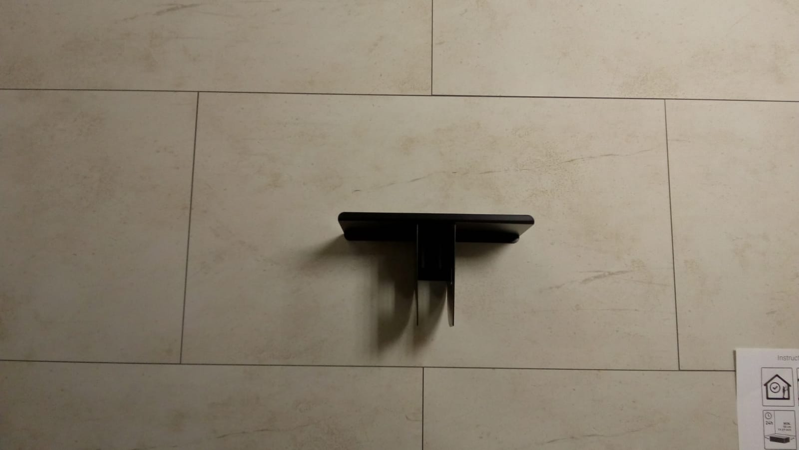 Black wall-mounted shelf centered on a beige tiled wall.