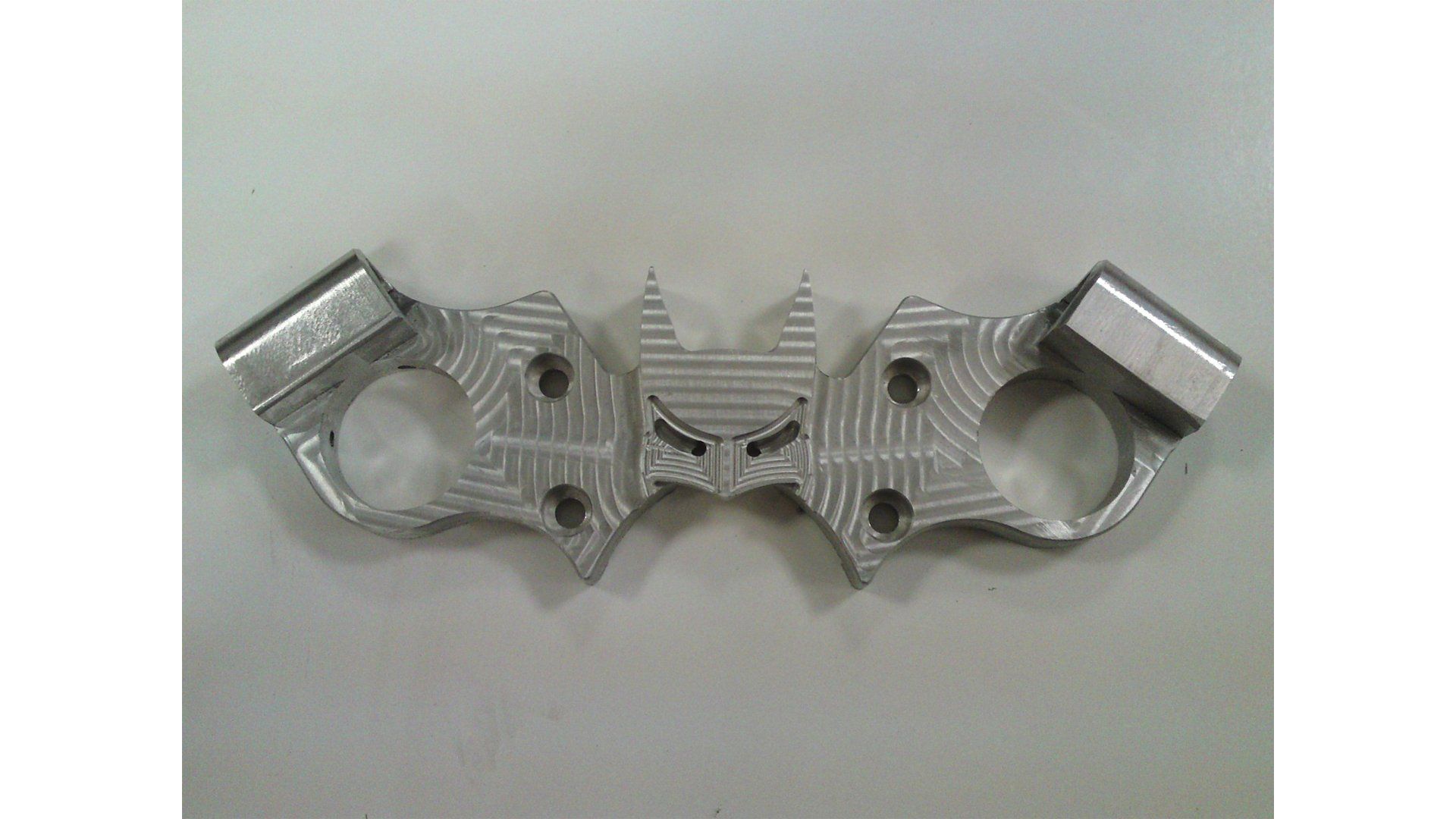 Silver metal mechanical part with two circular openings and angled ends on a plain background