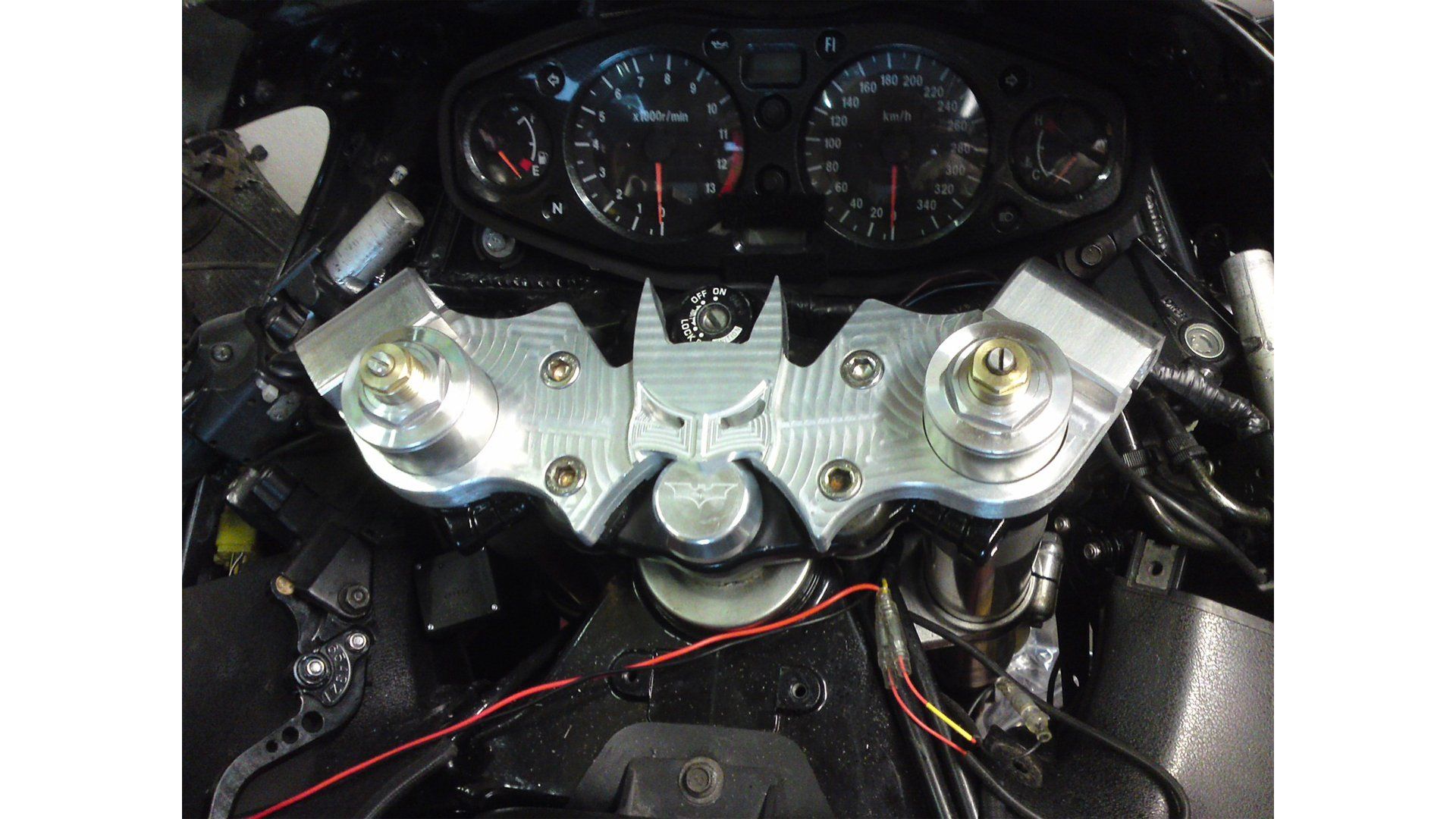Motorcycle cockpit with silver triple clamp and analog gauges viewed from the rider’s seat