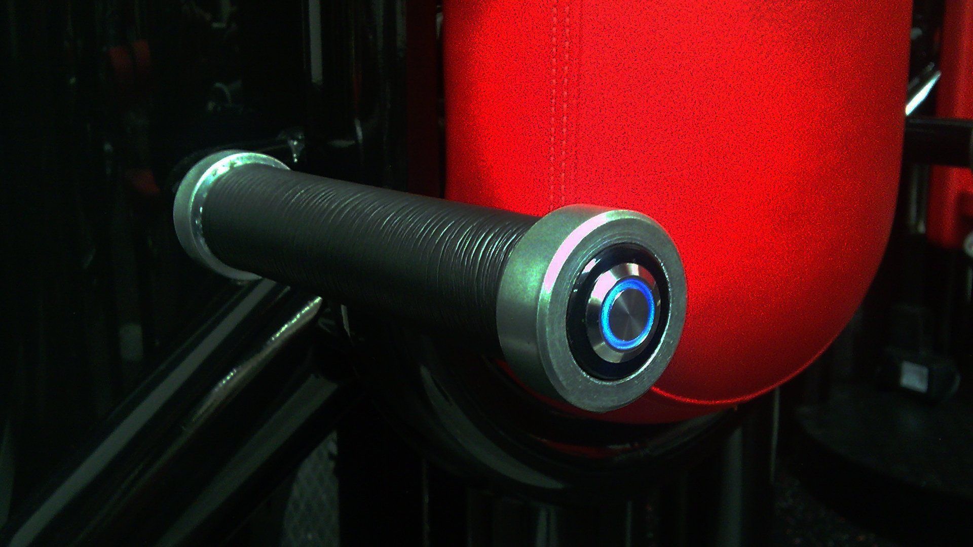 Close-up of a black cylindrical device with a glowing blue ring beside a red textured surface