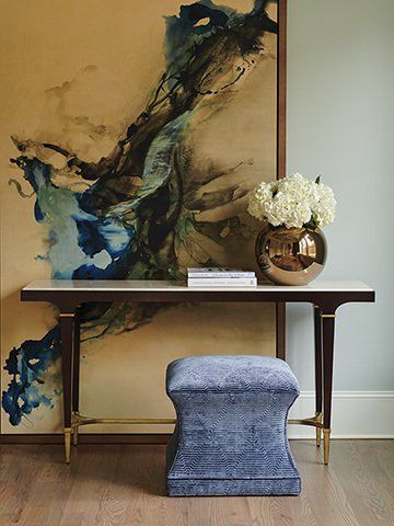 Table containing books, a vase, and a plant as home décor. Large decorative painting in the background