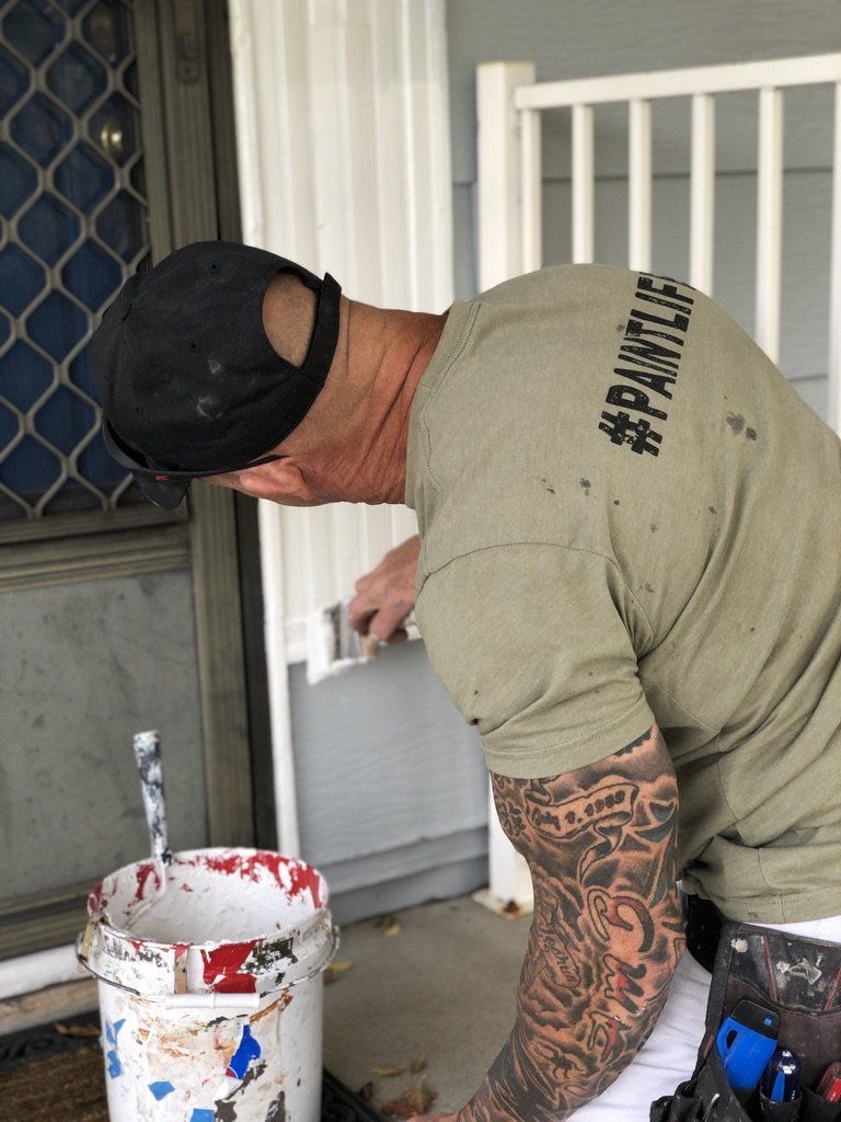 A man is painting a door with a brush and a bucket of paint.