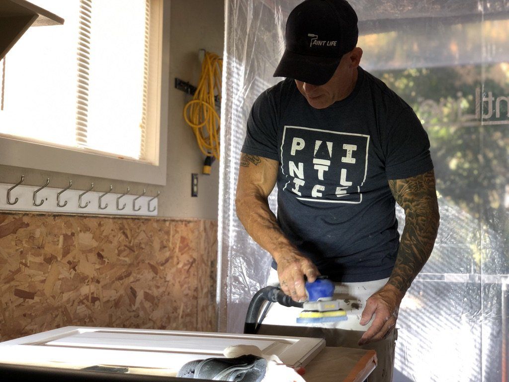 The Idaho Painter wearing a pai ntl tee is sanding a piece of wood.