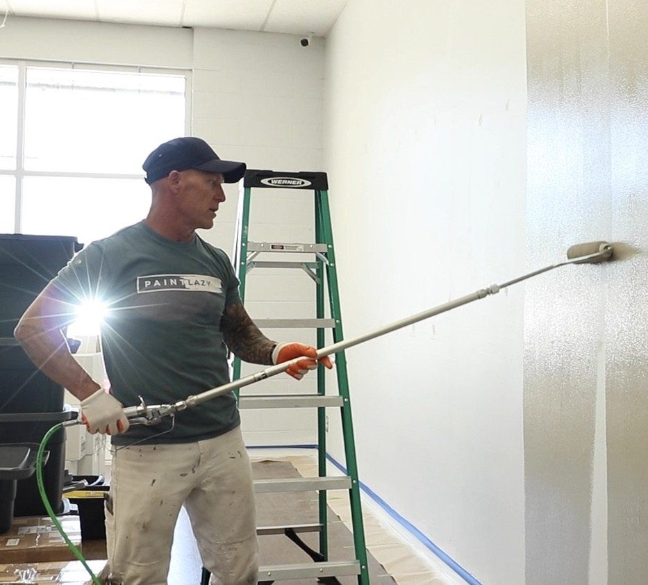 A man wearing a shirt that says paint on it is painting a wall