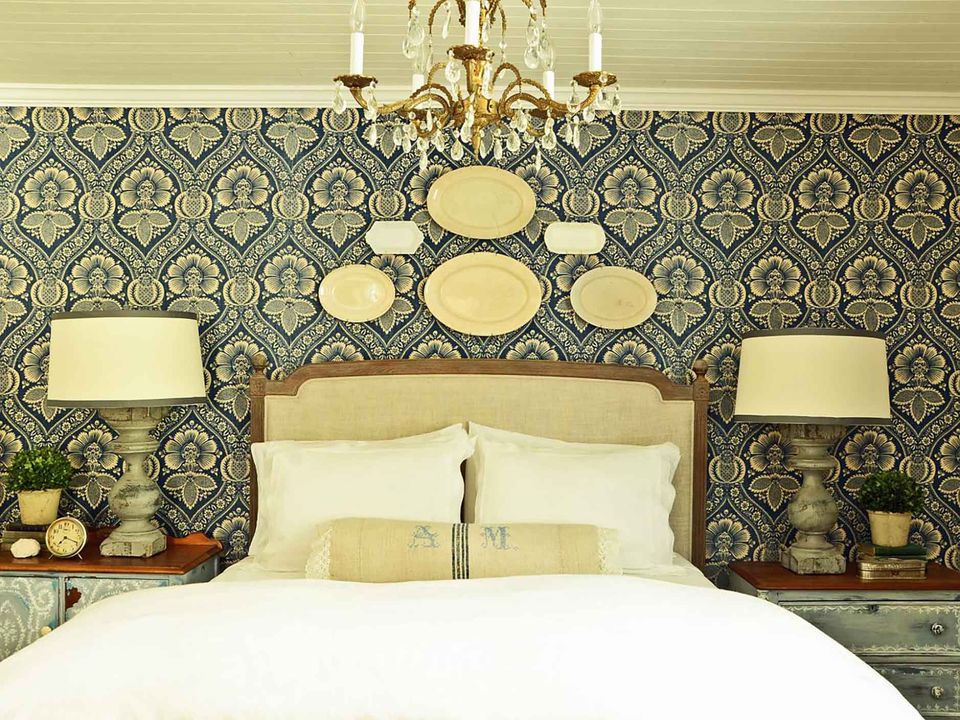 A bedroom with a white bed and a blue wallpaper with patterns.