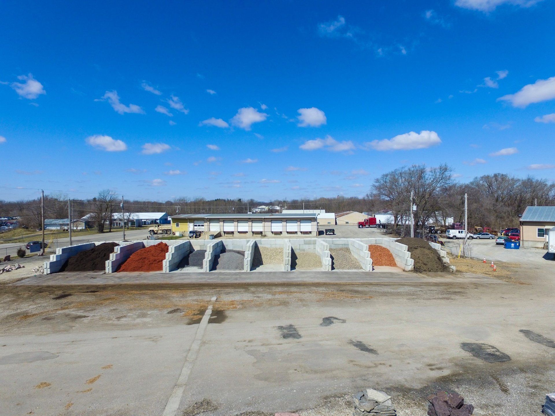 Exterior of a landscaping supply store, featuring piles of mulch and gravel under a blue sky.