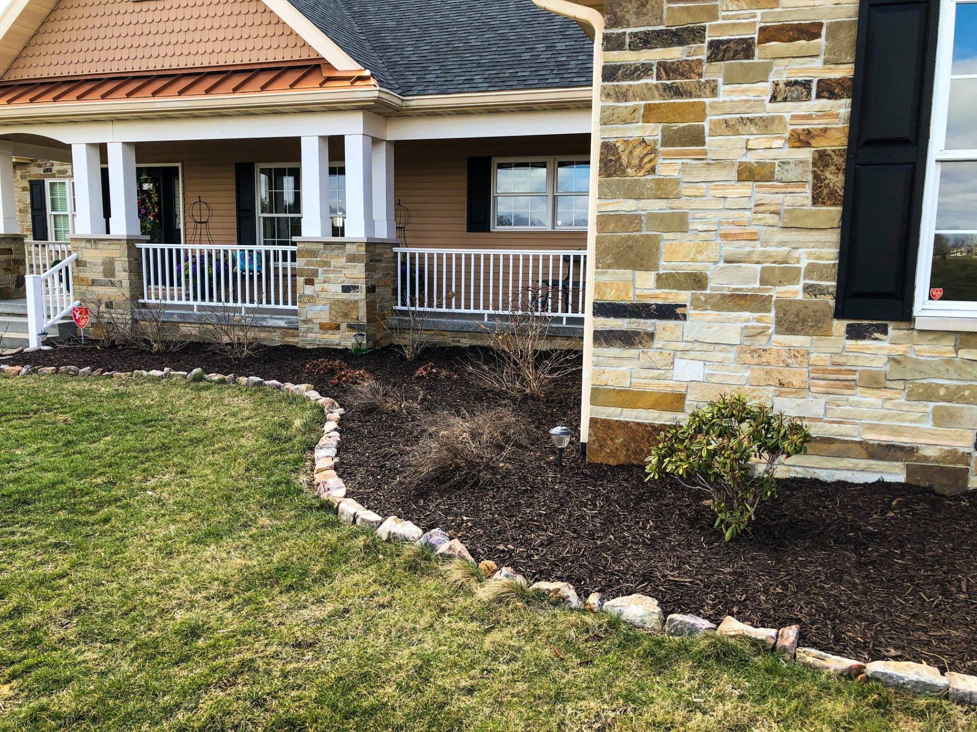 House exterior with stone facade, porch, and lawn edged with rocks and mulch.