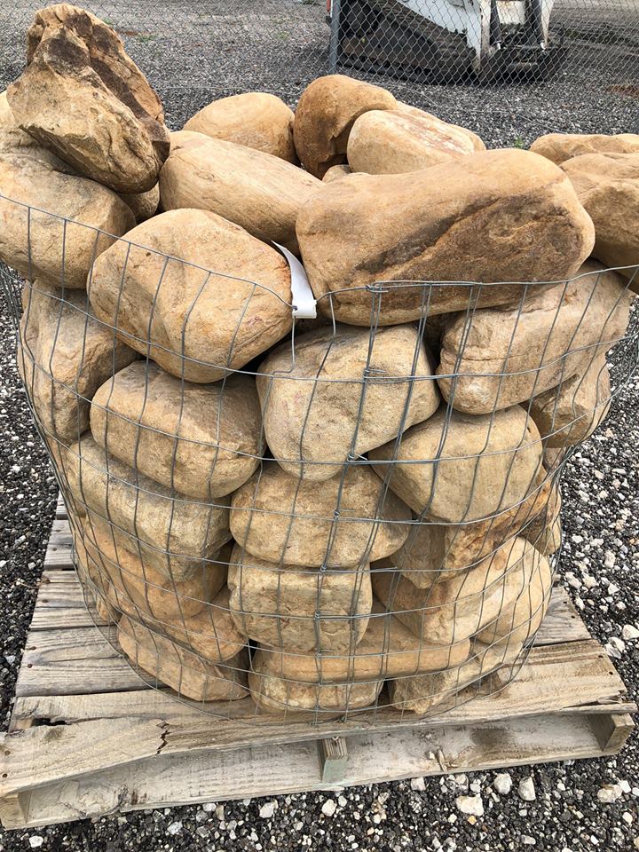 Large tan river rocks enclosed in wire mesh cage, on a wooden pallet.