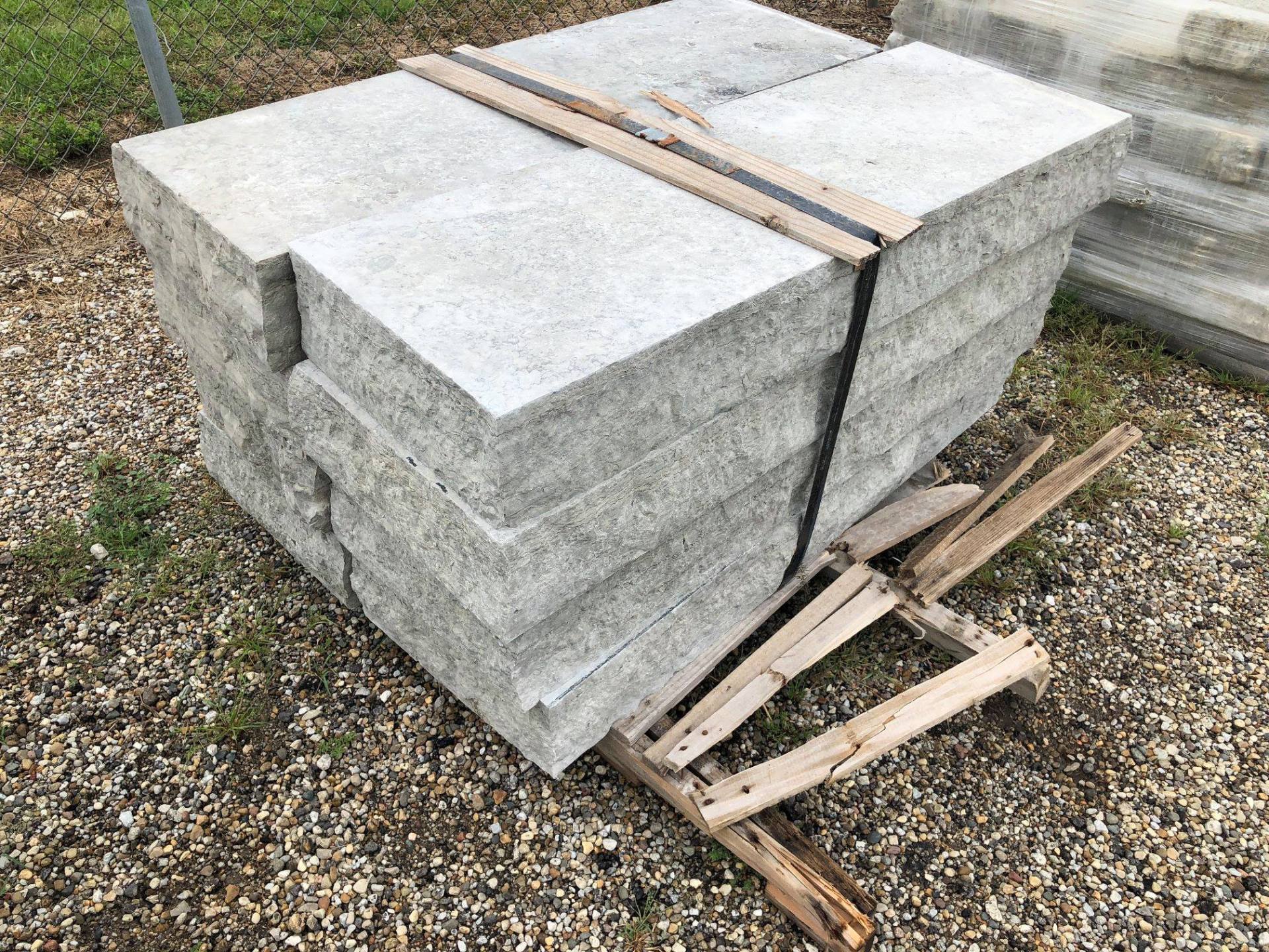 Stack of gray rectangular stone pavers bound with wooden slats on gravel.