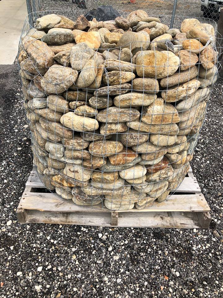 Round wire basket filled with beige and brown rocks on a wooden pallet.