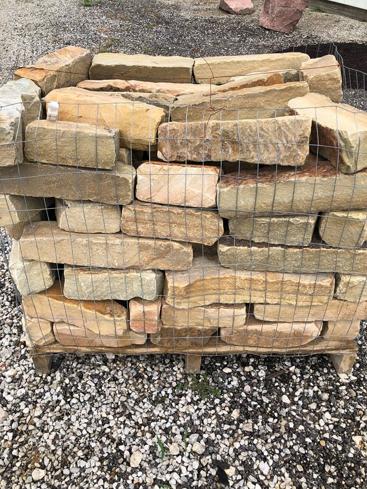 Pallet of tan rectangular sandstone blocks secured with wire mesh.