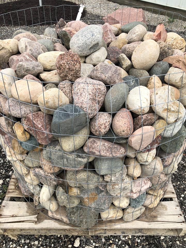 Rocks in various colors contained in a wire mesh basket on a wooden pallet.
