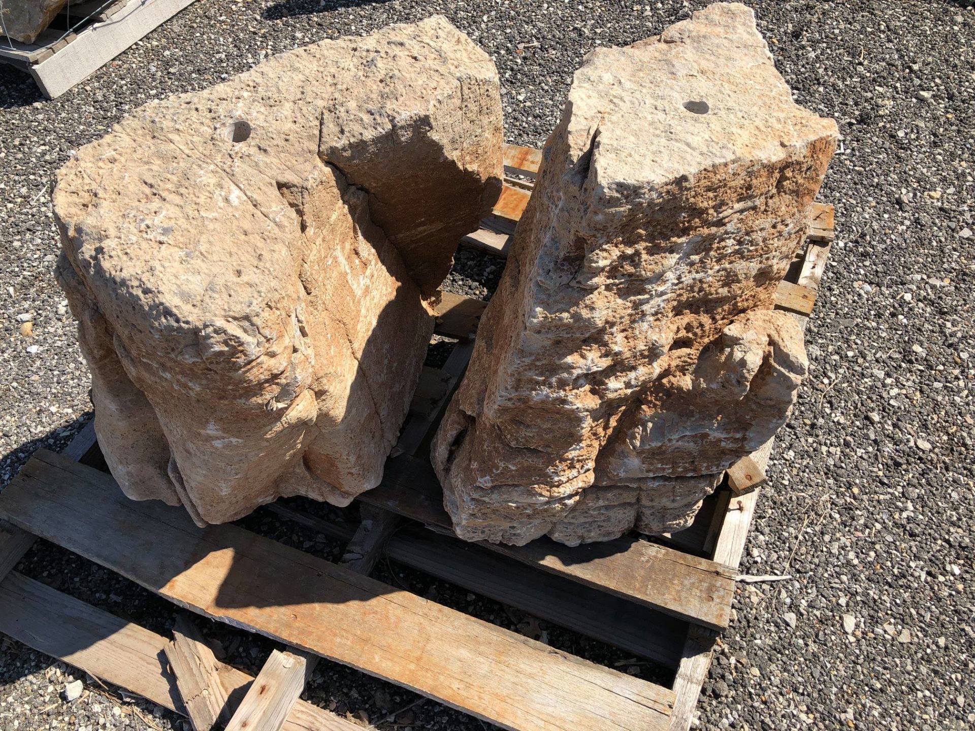 Two rough-cut sandstone blocks rest on a wooden pallet in an outdoor setting; tan color.