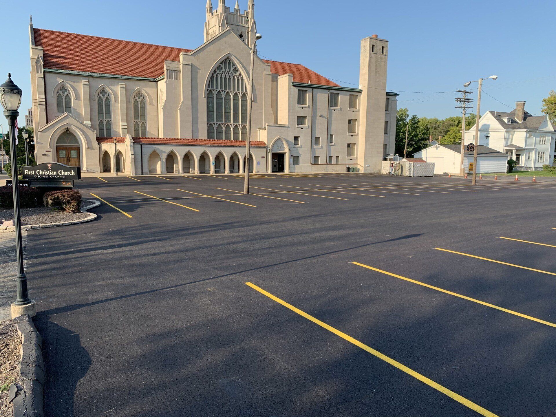 Church building with newly paved parking lot, light poles, and a small house in the background.