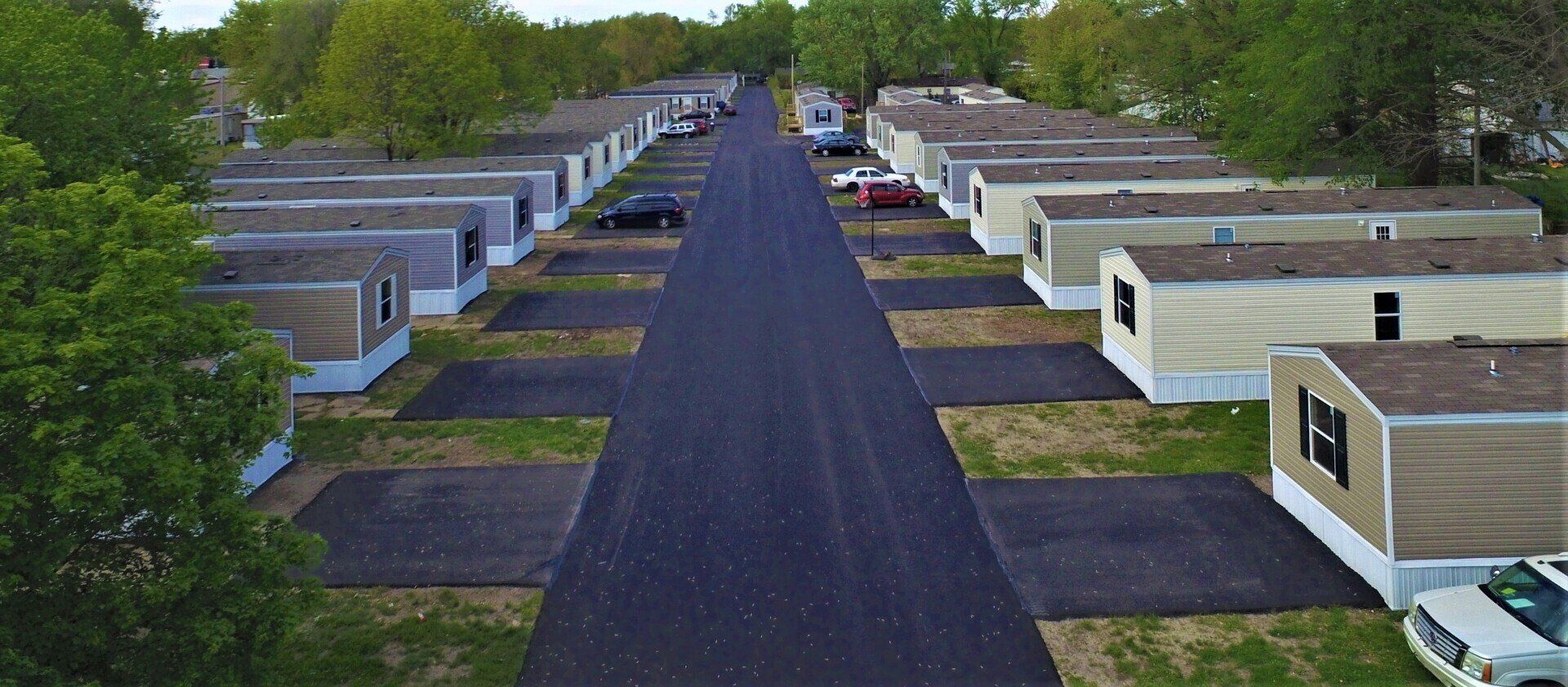 Aerial view of a mobile home park with a central paved road and parking spaces.