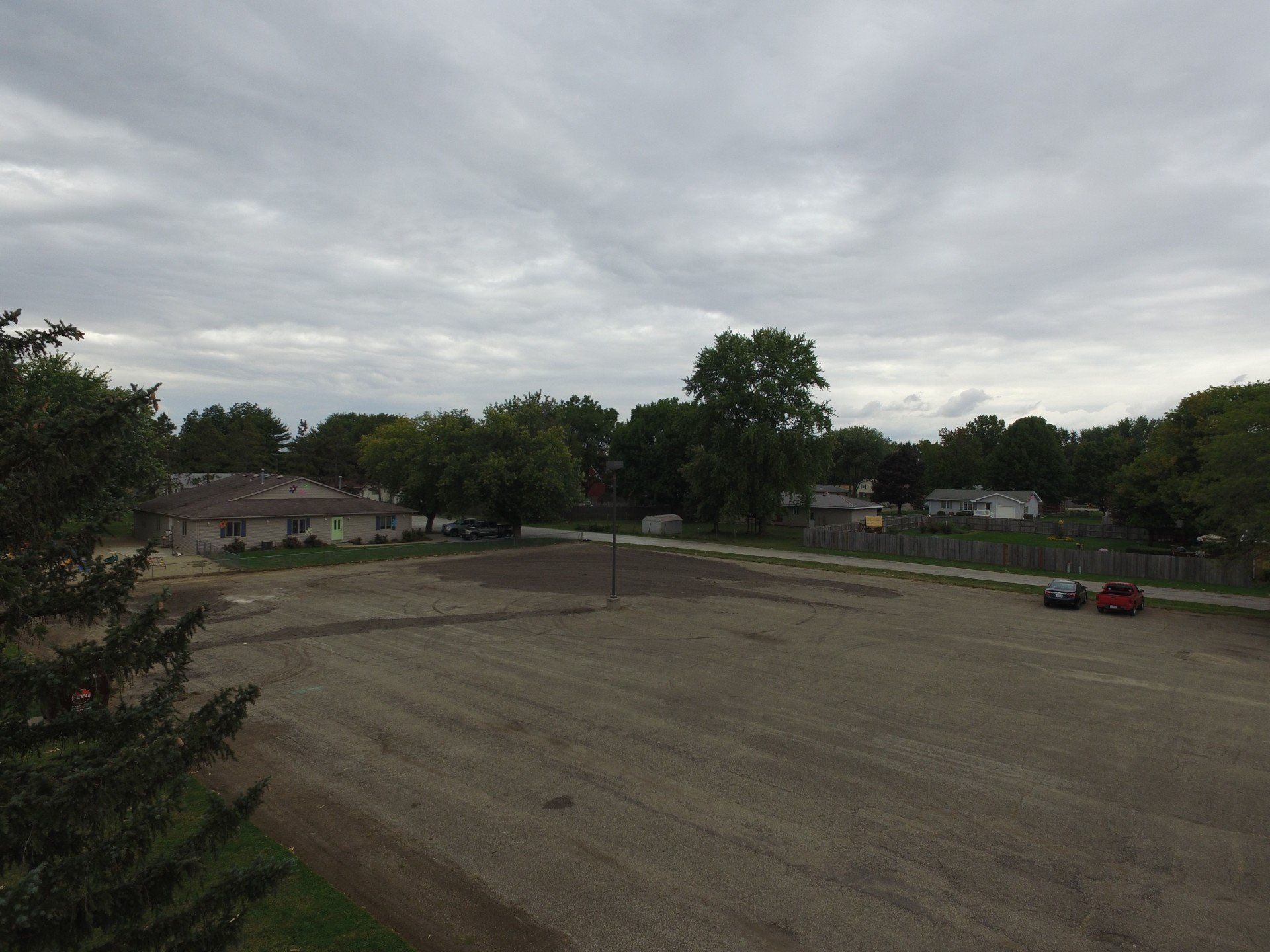 Gravel lot under overcast sky, with a few cars parked and houses in the background.