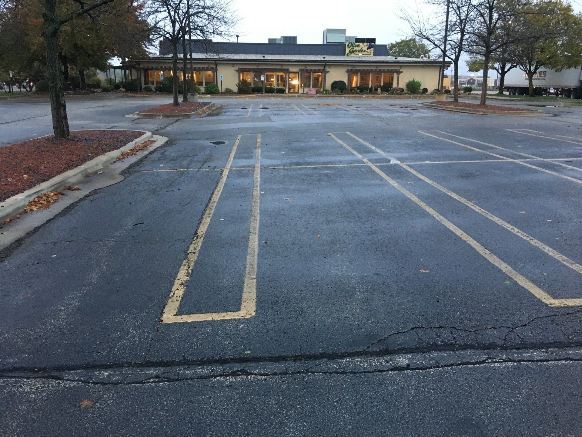 Empty parking lot with faded yellow lines, in front of a single-story building. Overcast day.