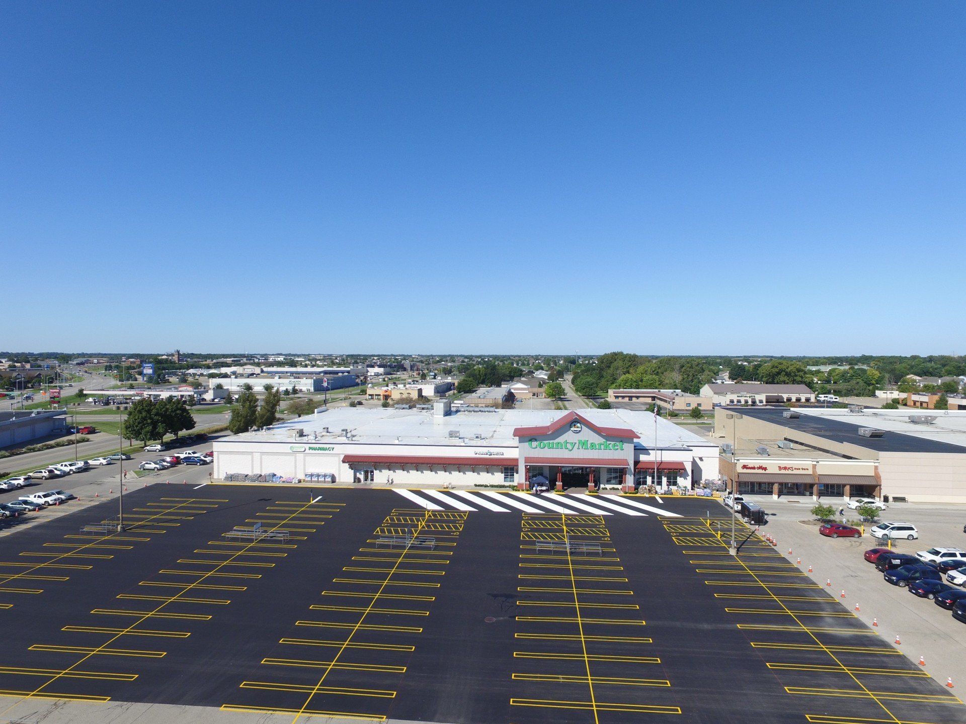 Aerial view of a large grocery store with a vast empty parking lot under a bright blue sky.