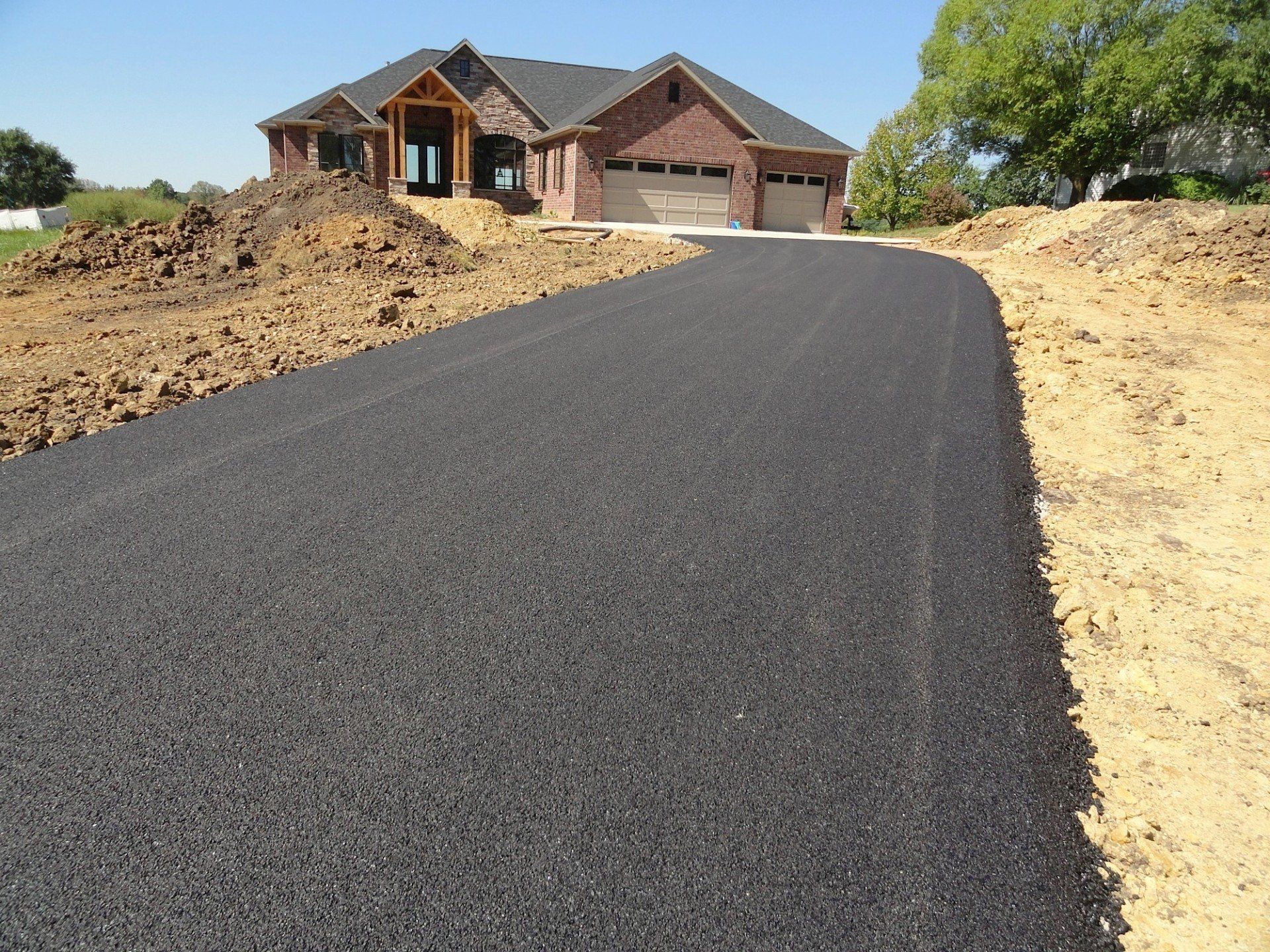 Newly paved asphalt driveway leading to a brick house under construction.