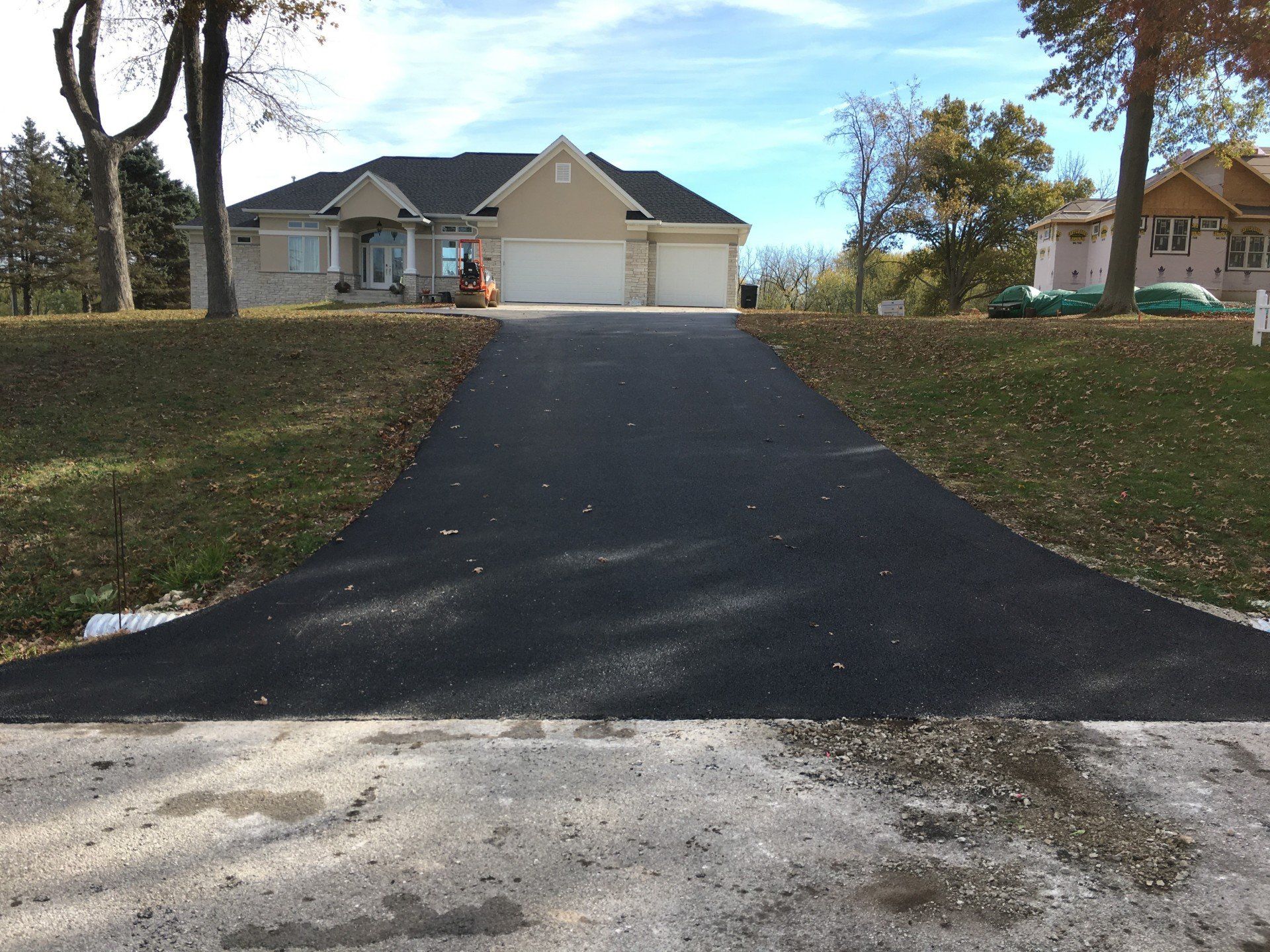 Asphalt driveway leading up to a beige house with a two-car garage under a sunny sky.