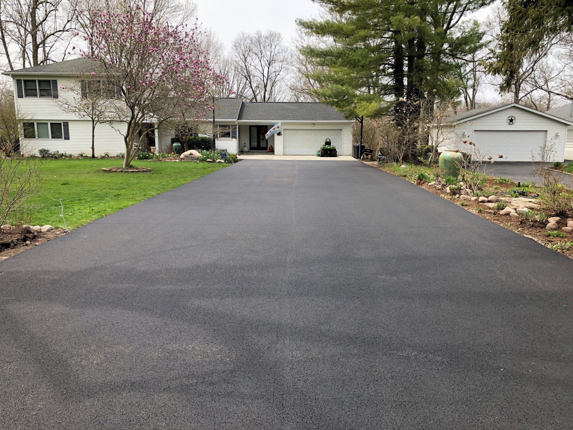 Paved asphalt driveway leading to a white two-story house with attached garage, in front of green lawn.