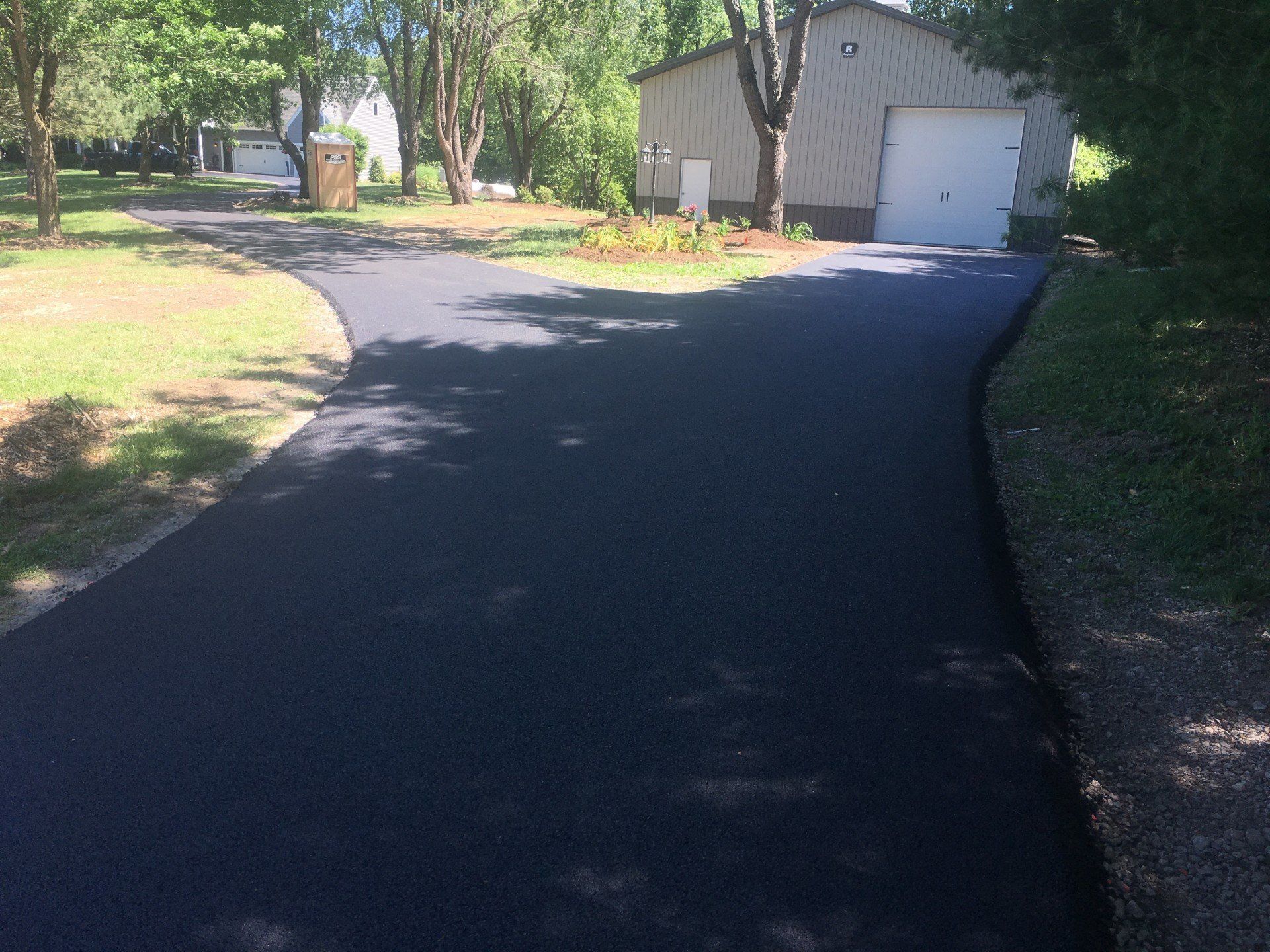 Newly paved black asphalt driveway curves towards a light-colored garage on a sunny day.