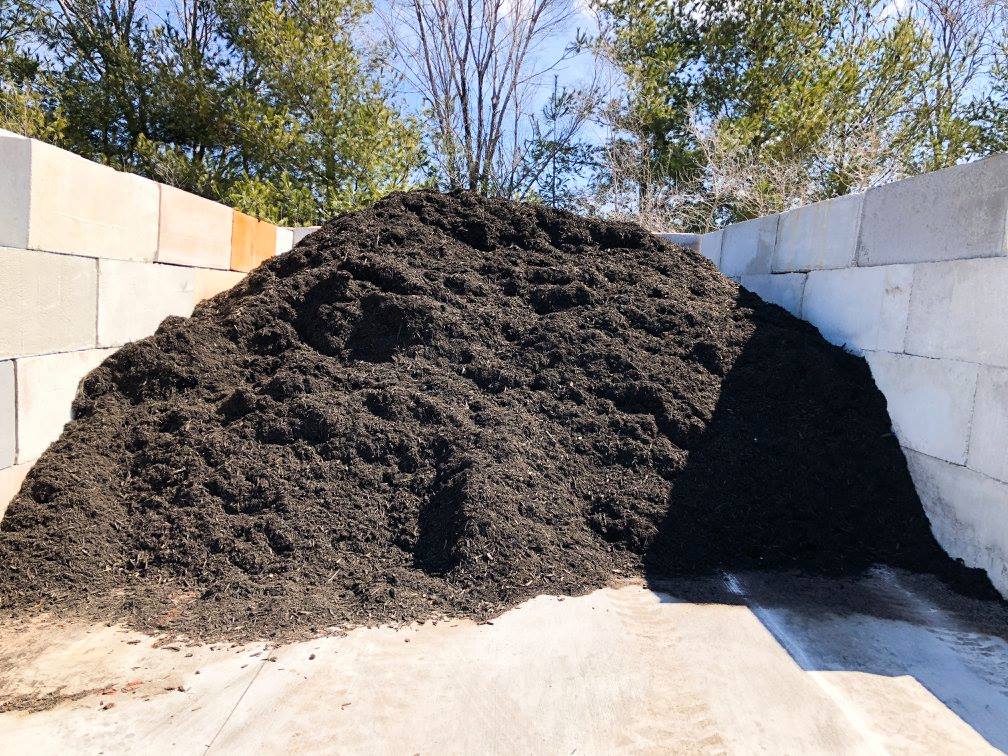 Mound of dark mulch enclosed by white and beige concrete blocks, outdoors under a sunny sky.